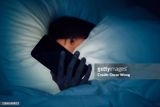 woman hiding under the blanketed and using smart phone at late night on bed - bullying stock pictures, royalty-free photos & images