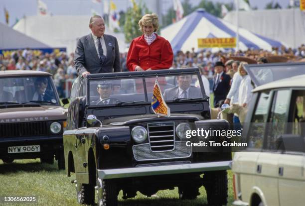 British Royal Diana, Princess Of Wales wearing a red suit, with a red polka dot blouse beneath a peplum jacket, riding with an unspecified man in an...