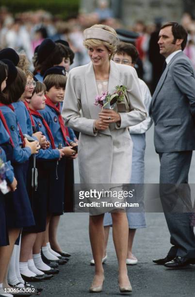 British Royal Diana, Princess of Wales , wearing a beige suit with a matching polka dot headband-style hat, carrying a bouquet of flowers as she...