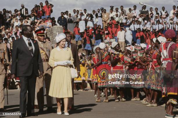 British Royal Queen Elizabeth II, wearing a yellow dress with a white collar, white evening gloves and a white hat, alongside President of Kenya...