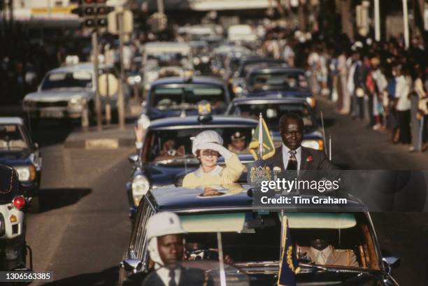 British Royal Queen Elizabeth II, wearing a yellow dress with a white collar, white evening gloves and a white hat, alongside President of Kenya...