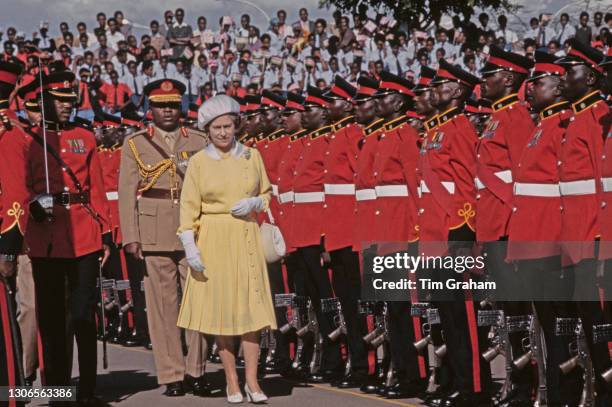 British Royal Queen Elizabeth II, wearing a yellow dress with a white collar, white evening gloves and a white hat, inspects an honour guard from...