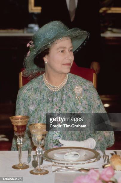 British Royal Queen Elizabeth II, wearing a green floral print outfit with a green hat and a pearl necklace, attends a luncheon in Tunis at the start...