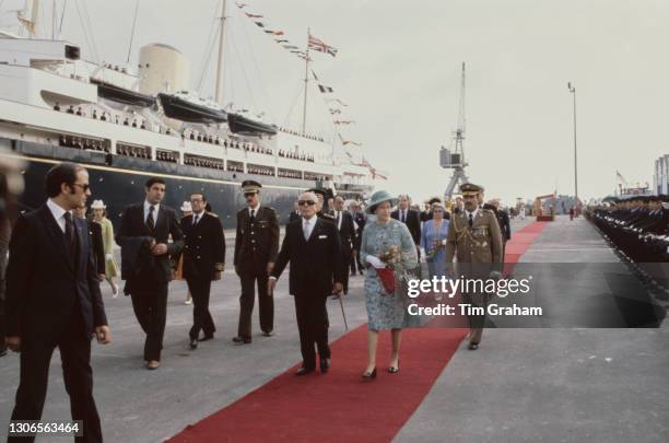 President of Tunisia Habib Bourguiba walks alongside British Royal Queen Elizabeth II, wearing a floral print outfit, as they walk the red carpet...