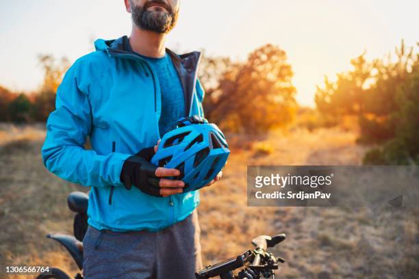 nahaufnahme eines männlichen bikers, der seinen fahrradhelm hält und sich ausruht - cycling helmet stock-fotos und bilder