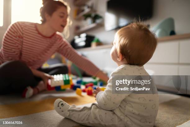 achter mening van een zitting van de babyjongen op de vloer, die pret met speelgoed heeft en zijn moeder bekijkt - boy sitting on floor stockfoto's en -beelden