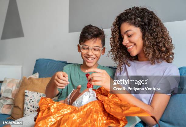 siblings eating easter egg on sofa - eating chocolate easter egg stock pictures, royalty-free photos & images
