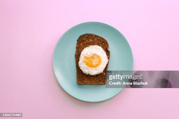 fried egg on dark toasted bread on blue plate over pink background. concept of vegetarian breakfast or lunch. - stekt ägg bildbanksfoton och bilder