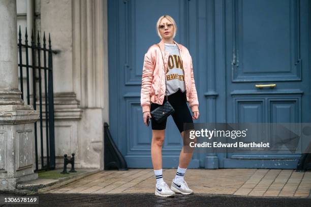 Emy Venturini wears sunglasses, a pink shiny bomber jacket from Finders, a gray sweater, black short leggings from Alesia Concept, a black quilted...