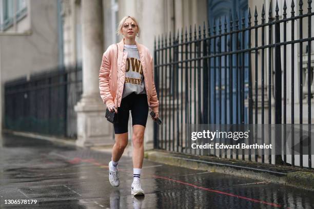 Emy Venturini wears sunglasses, a pink shiny bomber jacket from Finders, a gray sweater, black short leggings from Alesia Concept, a black quilted...