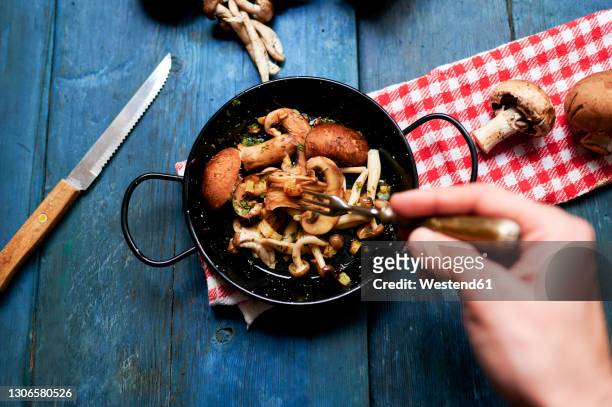 hand of man eating pan of fried mushrooms - shiitake mushroom stock pictures, royalty-free photos & images