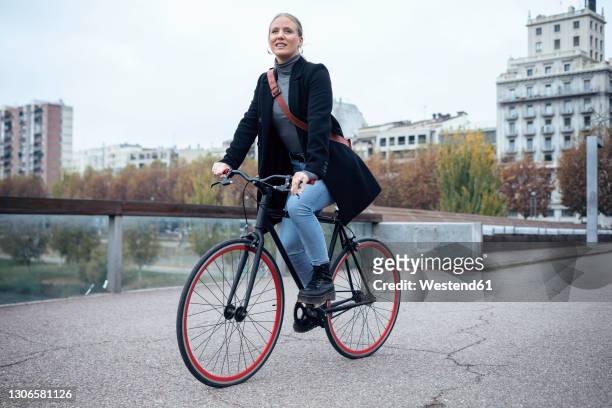 smiling woman cycling on road against sky - woman on bicycle stock pictures, royalty-free photos & images