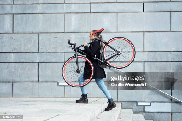 woman carrying cycle while walking on staircase by wall - carrying bike stock pictures, royalty-free photos & images