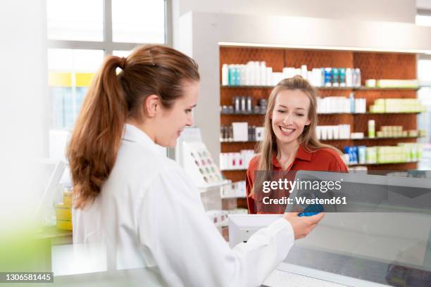 female pharmacist reading instructions on medicine while woman standing at checkout - apothekerin stock-fotos und bilder