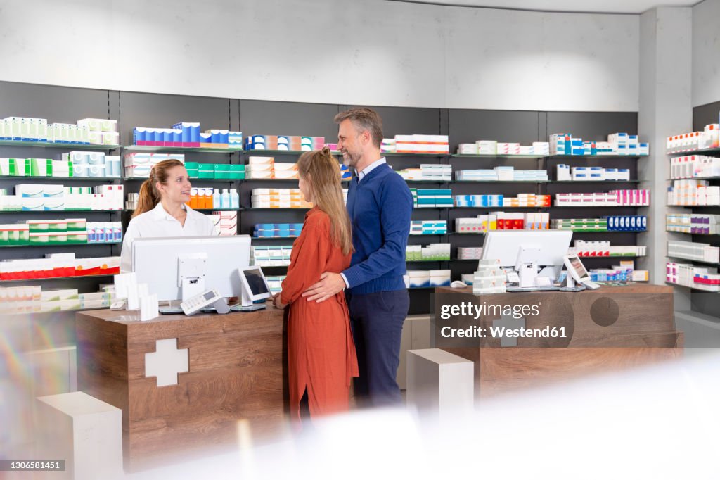 Couple talking to female pharmacist at pharmacy checkout