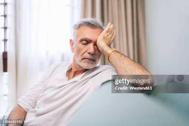 tired man rubbing eyes while sitting on sofa in hotel room - stanchezza foto e immagini stock