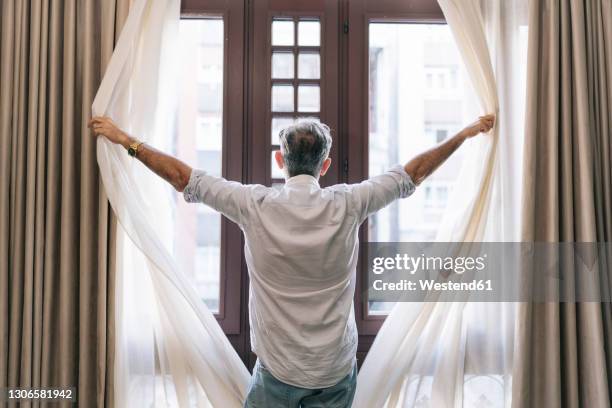 man opening curtains in hotel room - opening the curtains stock pictures, royalty-free photos & images