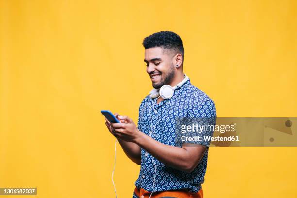 smiling man using mobile phone by yellow background - man holding phone stock pictures, royalty-free photos & images