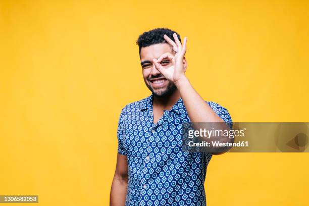 happy man showing ok gesture while standing against yellow background - ok zeichen stock-fotos und bilder