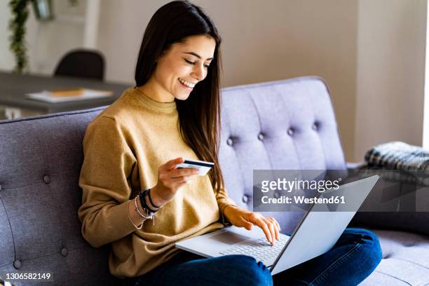 young woman with credit card shopping over laptop while sitting at home - onlinebanking stock-fotos und bilder