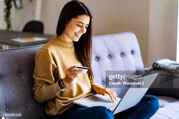 young woman with credit card shopping over laptop while sitting at home - ホームショッピング ストックフォトと画像