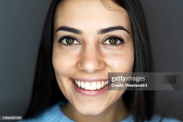 close-up of woman with reflection of circular strobe in eyes smiling while standing against gray background - front flash photography foto e immagini stock