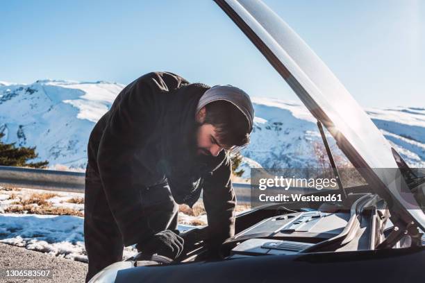 man repairing car on snow covered land against sky during winter - winter panne auto stock-fotos und bilder