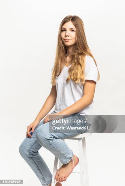 pre-adolescent girl sitting on stool against white background in studio - 12 year old blonde girl stock pictures, royalty-free photos & images