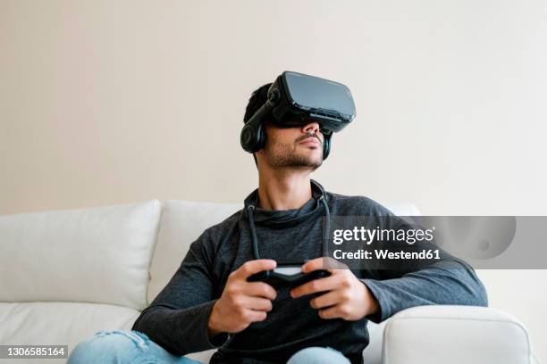 young man playing video game through virtual reality simulator - virtual reality gaming stock pictures, royalty-free photos & images