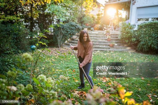 happy woman sweeping garden with broom in back yard - rechen stock-fotos und bilder