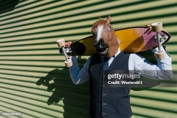 businessman in horse mask holding longboard behind head against wall - behind the green horse stock pictures, royalty-free photos & images