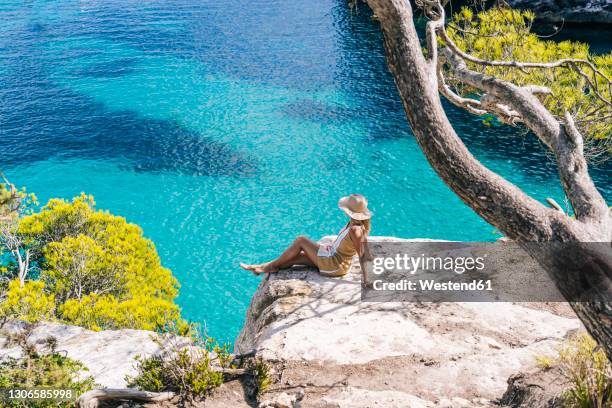 woman sitting on rock by sea during sunny day - minorca stock-fotos und bilder