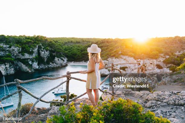 woman looking at sunset while leaning on railing at beach - islas baleares fotografías e imágenes de stock