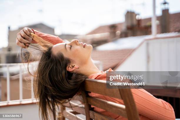 woman playing with hair while relaxing on chair at rooftop - hair imagens e fotografias de stock