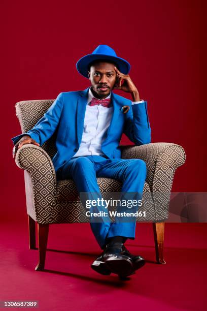 mid adult man with head in hand sitting on chair against red background - hat and suit stock pictures, royalty-free photos & images