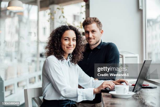 confident businesswoman sitting by colleague with laptop at cafe - portrait femme business photos et images de collection