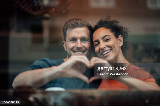 smiling couple making heart with hand while sitting by cafe window - two hearts fotografías e imágenes de stock