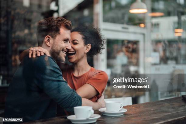 cheerful woman sitting with arm around on man at cafe - lachen stock-fotos und bilder