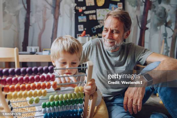 happy father watching son counting abacus in bedroom - abacus stock-fotos und bilder