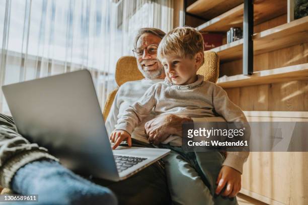 boy using laptop while sitting with father on chair - familie laptop stock-fotos und bilder