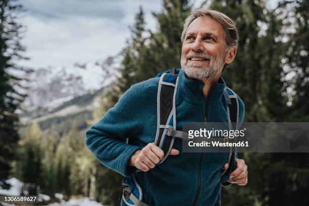smiling mature man looking away while hiking in forest at salzburger land, austria - hiking backpack stock-fotos und bilder