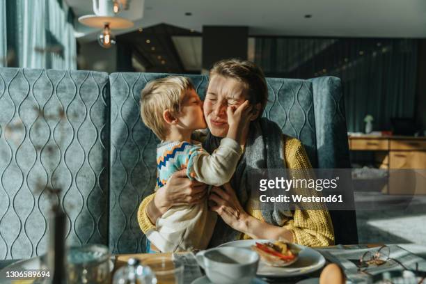 son kissing mother while sitting at table in hotel room - family holidays hotel stock pictures, royalty-free photos & images