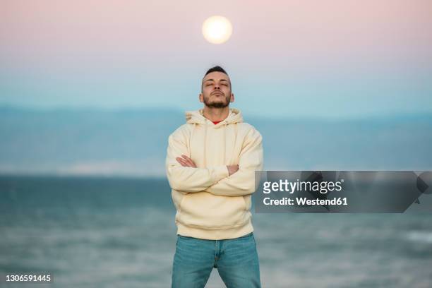 mid adult man standing with eyes closed and arms crossed against moon - hooded shirt ストックフォトと画像