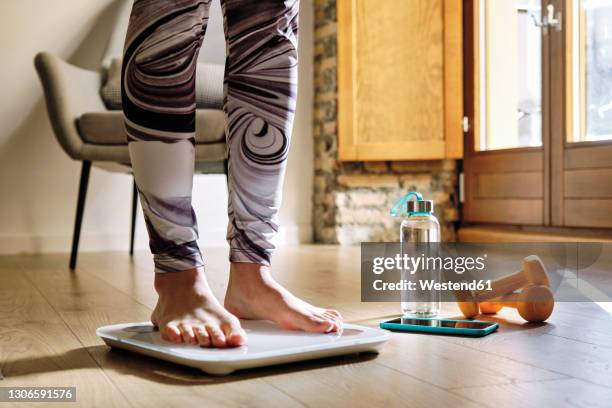 woman analyzing weight while standing on weight scale at home - scale fotografías e imágenes de stock