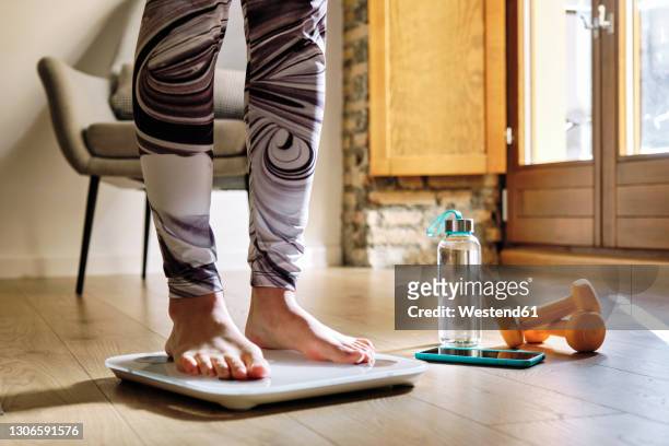 woman analyzing weight while standing on weight scale at home - weight scale foto e immagini stock
