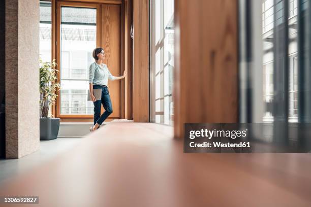 businesswoman with laptop looking through window at office - alleen één oudere vrouw stockfoto's en -beelden