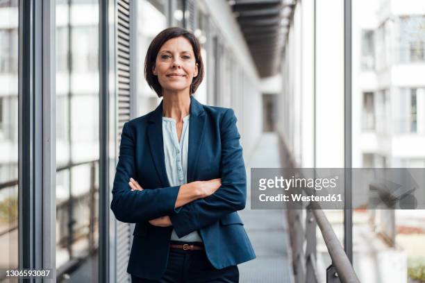 smiling confident businesswoman with arms crossed standing on balcony - femme d'affaires photos et images de collection