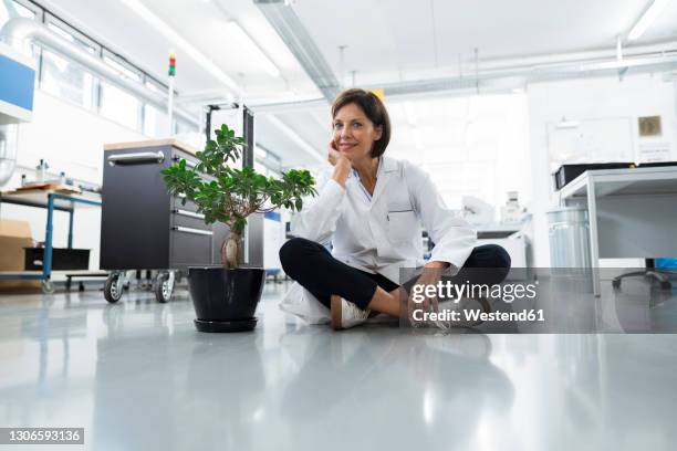 female engineer with hand on chin sitting on floor in industry - schneidersitz stock-fotos und bilder