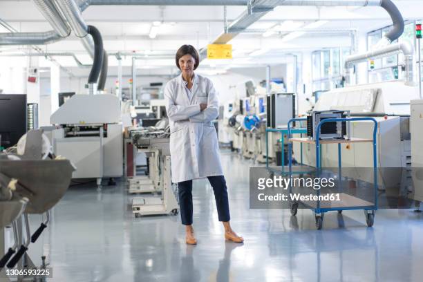 confident female engineer with arms crossed standing in industry - laboratory coat stock-fotos und bilder