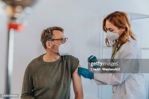 general practitioner injecting covid-19 vaccine in patient arm while standing at examination room - doctor general practitioner stock pictures, royalty-free photos & images